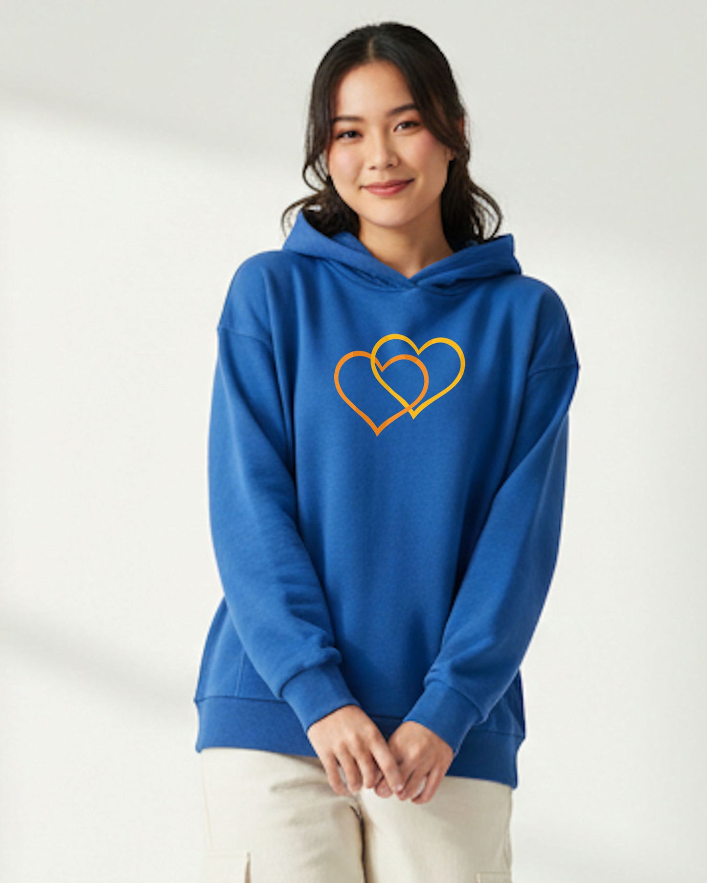 Woman wearing a blue hoodie with a dual orange and yellow heart design on a white background