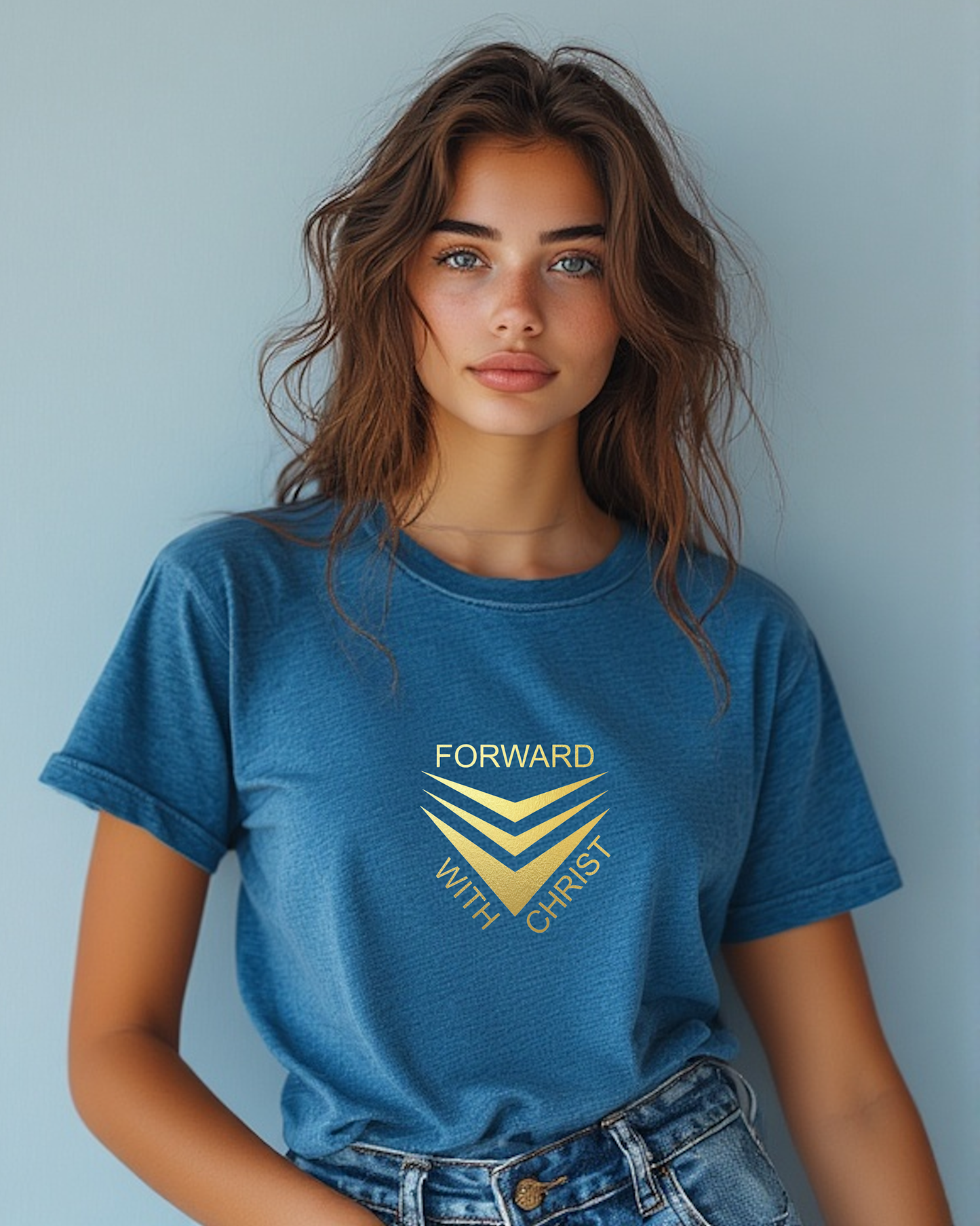 A woman standing wearing a blue short sleeve t-shirt that has a gold logo with the words "FORWARD WITH CHRIST" around 3 downward pointing chevrons.