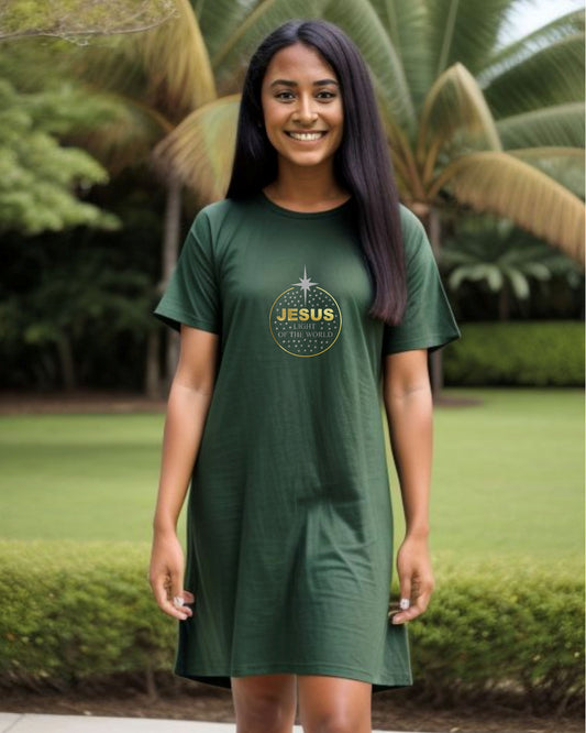 A woman in a garden wearing a dark green t-shirt dress with a gold text logo "Jesus" and silver text, "light of the world" within a gold circle containing silver stars.