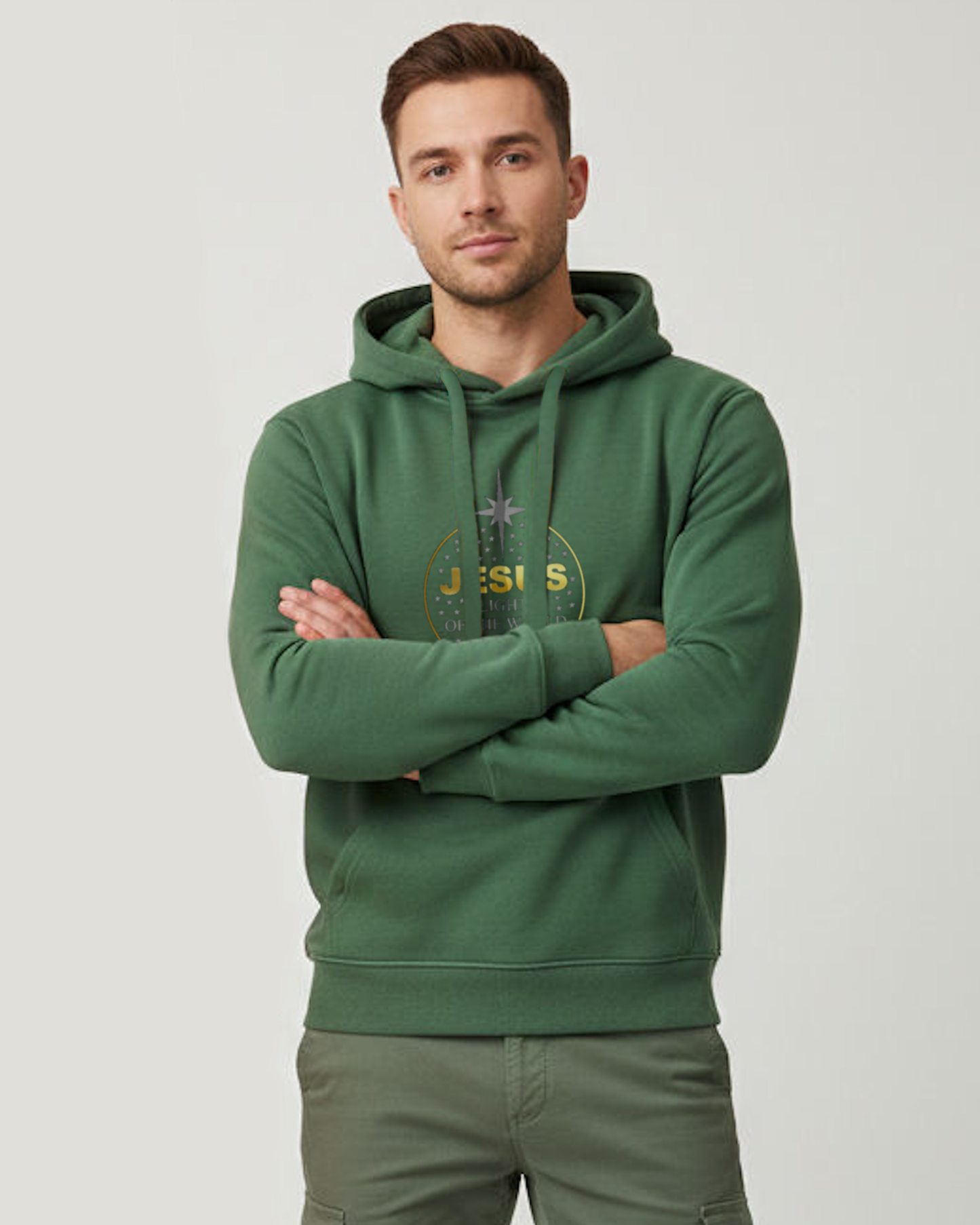 A man standing indoors wearing a green hoodie with a gold/silver text and graphic logo. The text reads 'Jesus light of the World'