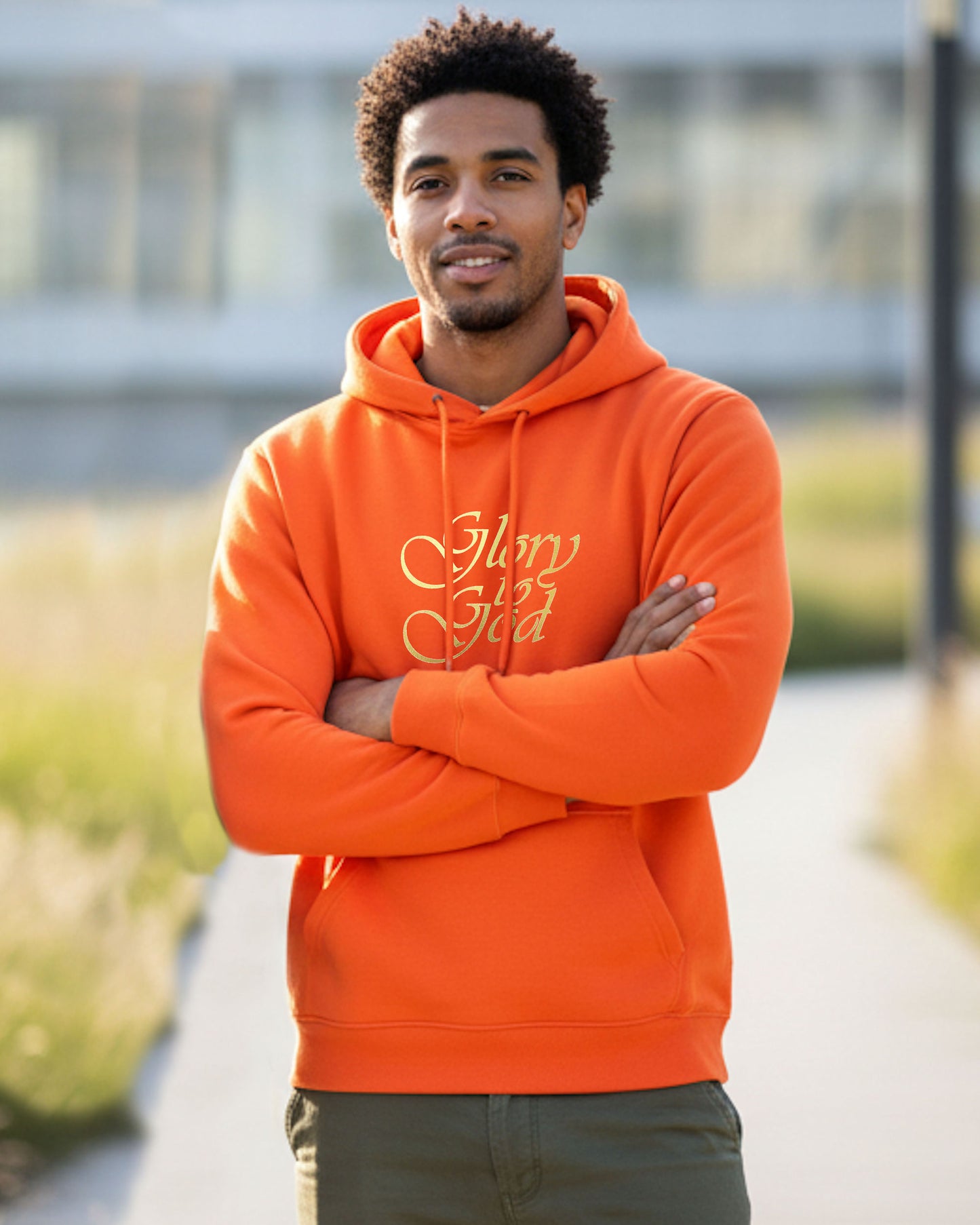 Man wearing an orange hoodie with gold text, 'Glory to God', standing outdoors.