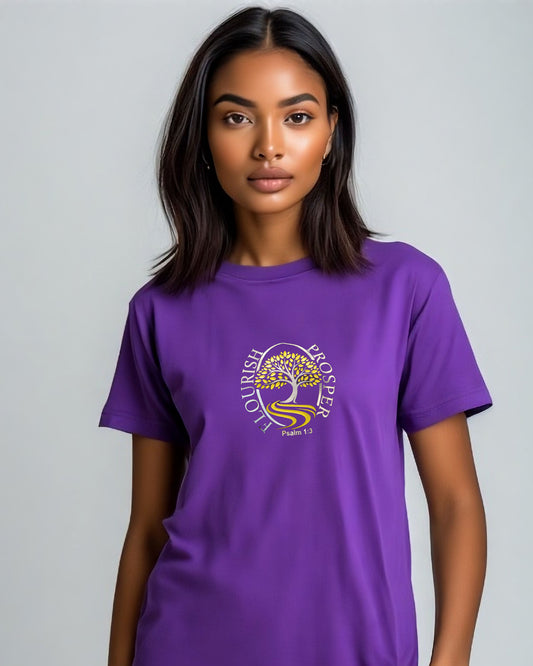 Woman wearing a purple t-shirt with a gold and silver logo (Flourish Prosper) in a bedroom setting