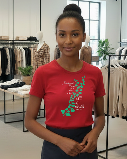 A woman wearing a red graphic t-shirt with a green vine design and white cursive text 'Jesus said I am the vine you are the branches', standing inside a clothing store.