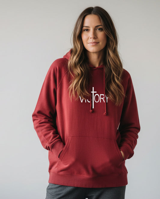 A young woman wearing a red hoodie with a white Heavenly Dreamwear "Victory" logo printed on front against a plain grey background.
