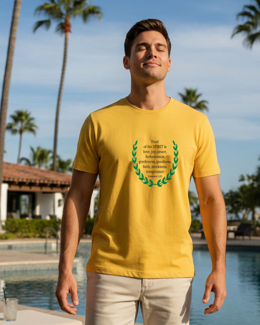 Man wearing a yellow t-shirt with a black text and green laurel wreath design by a pool with palm trees in the background.