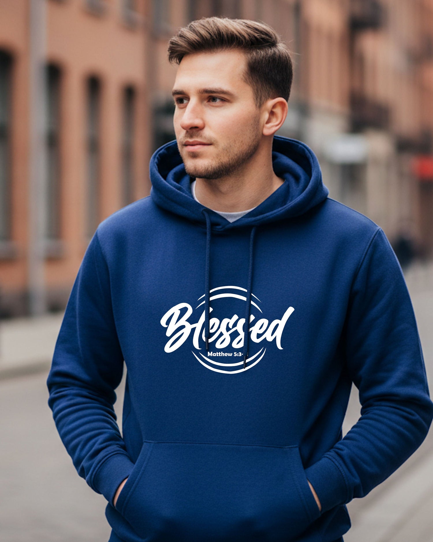 A man standing in a street wearing ablue hoodie with a Heavenly Dreamwear "Blessed" logo printed onthe front.
