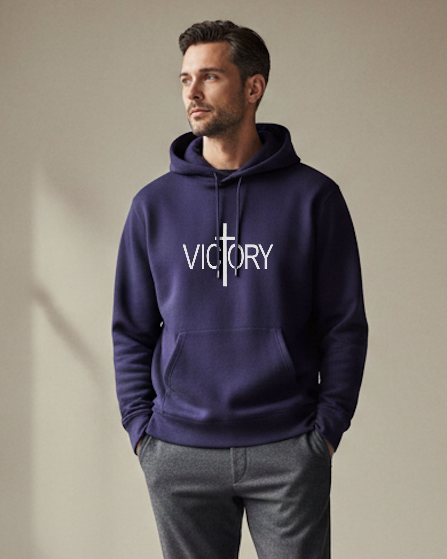 A young man indoors wearing a navy blue hoodie with a white Heavenly Dreamwear "Victory" logo printed on front.