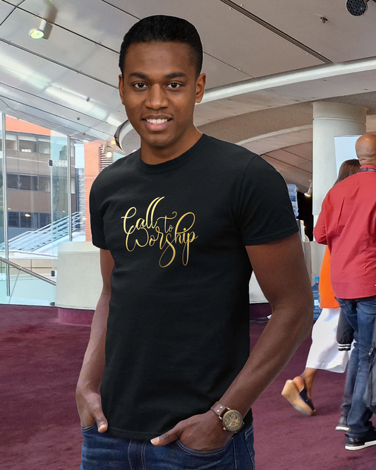 A man standing in convention centre wearing a black t-shirt with a Heavenly Dreamwear designed "Calll to Worship" logo printed in gold on the front.