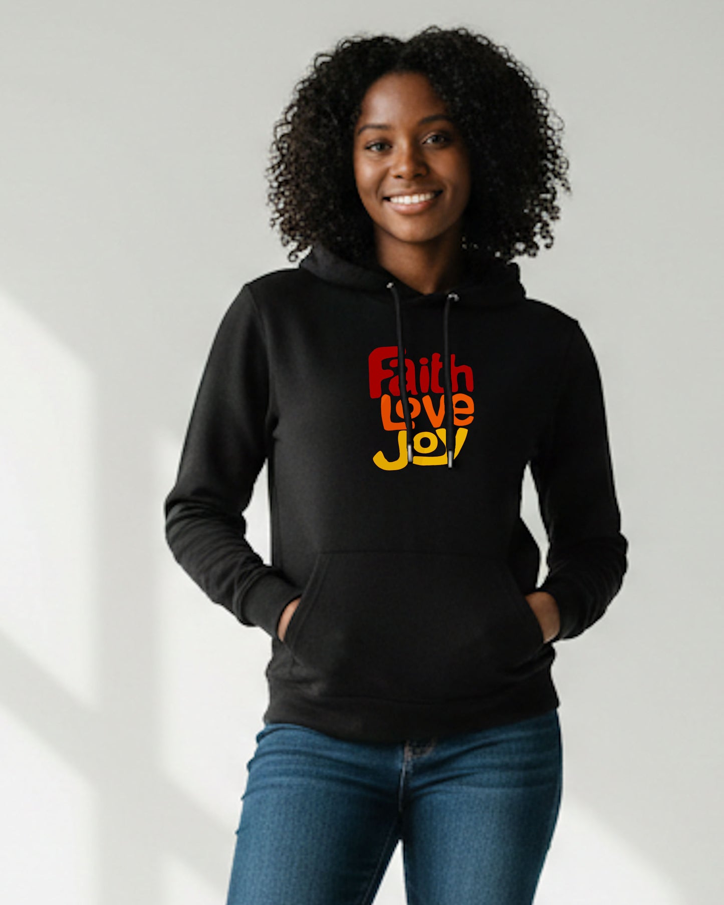 Woman standing against a white background wearing a black hoodie with a red, orange and yellow Heavenly Dreamwear text logo printed on the front. 