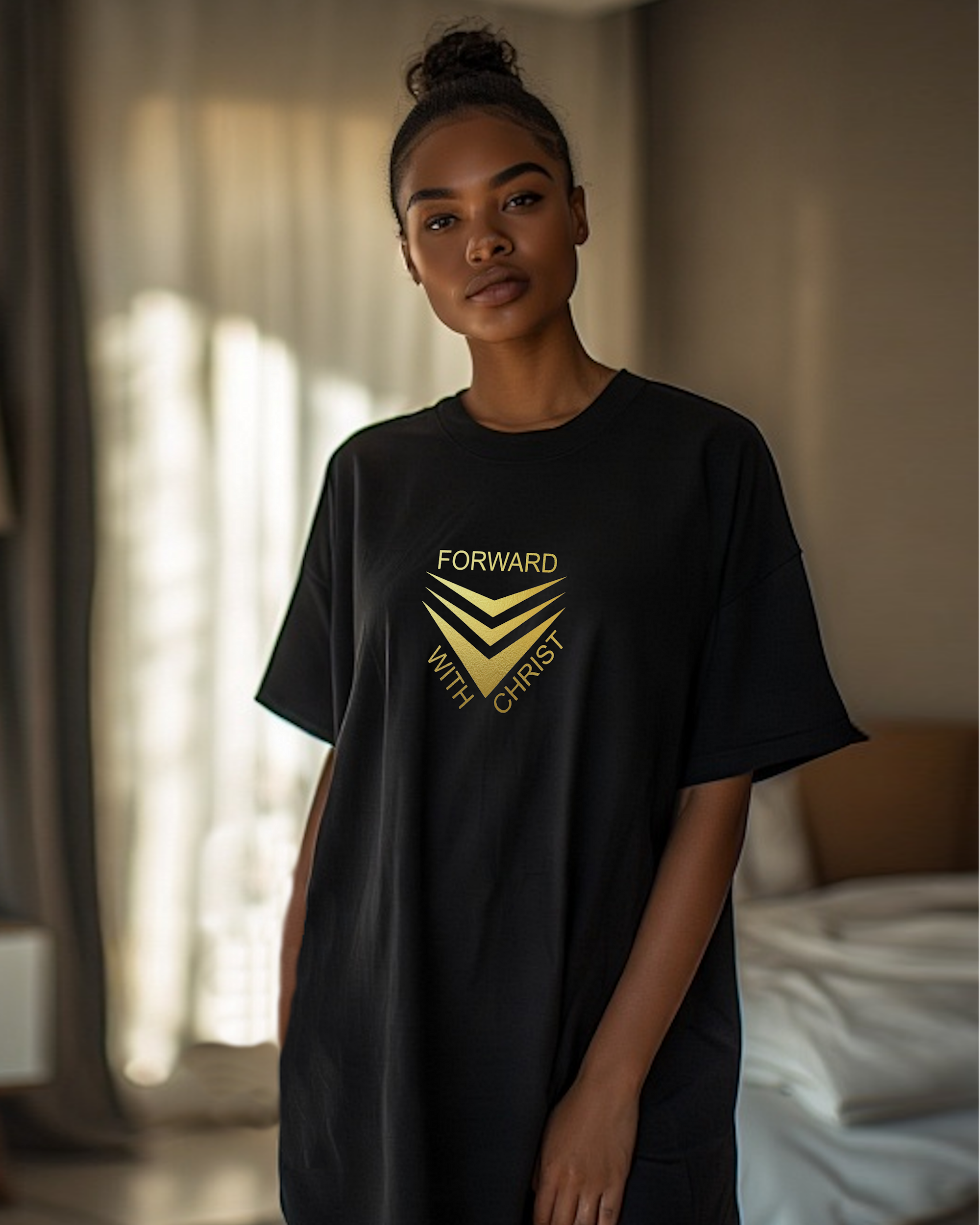 A woman standing in a bedroom wearing a black short sleeve t-shirt that has a gold logo with the words "FORWARD WITH CHRIST" around 3 downward pointing chevrons.