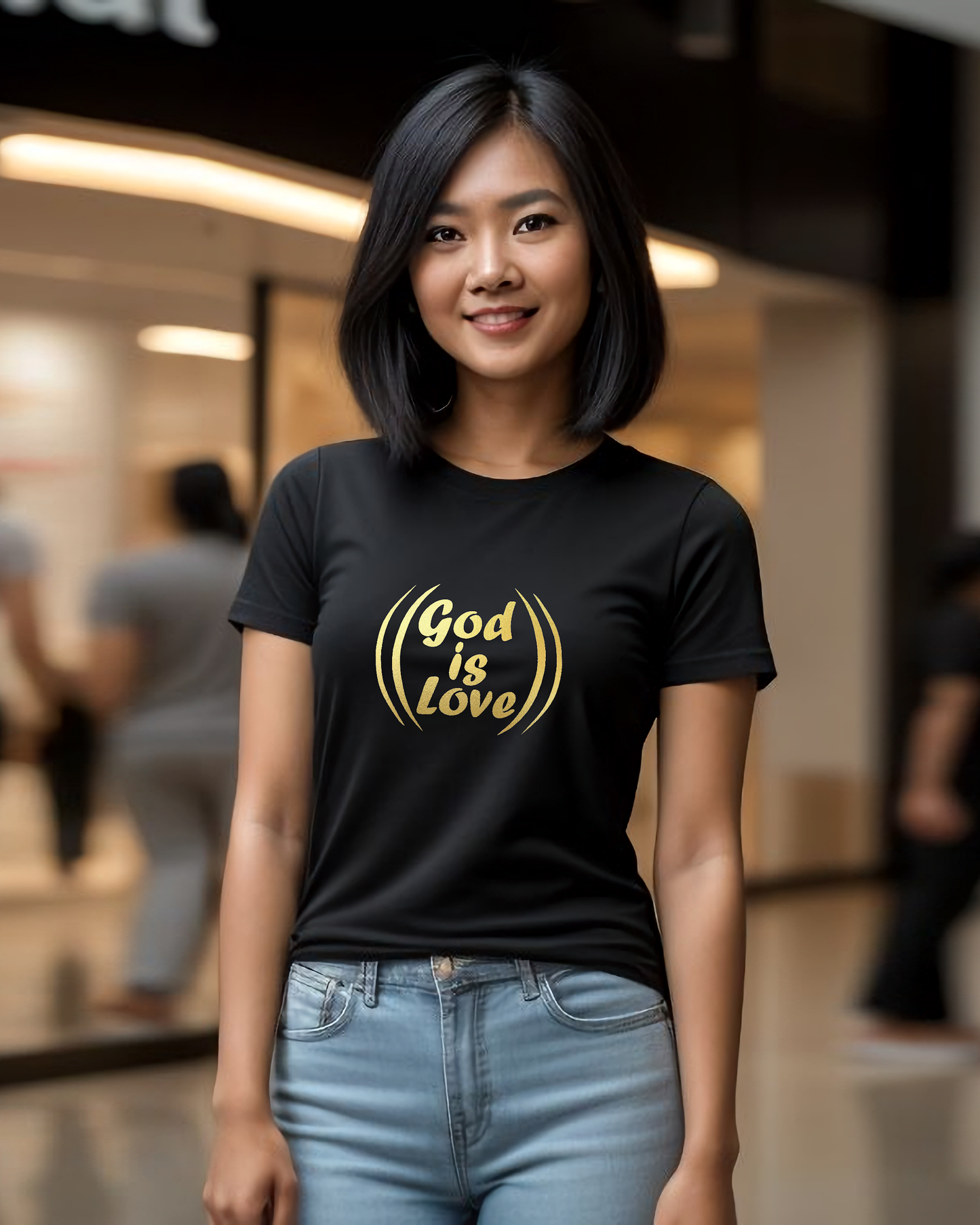 A woman in a shopping mall wearing a black t-shirt with a gold "God is Love" logo printed on the front.