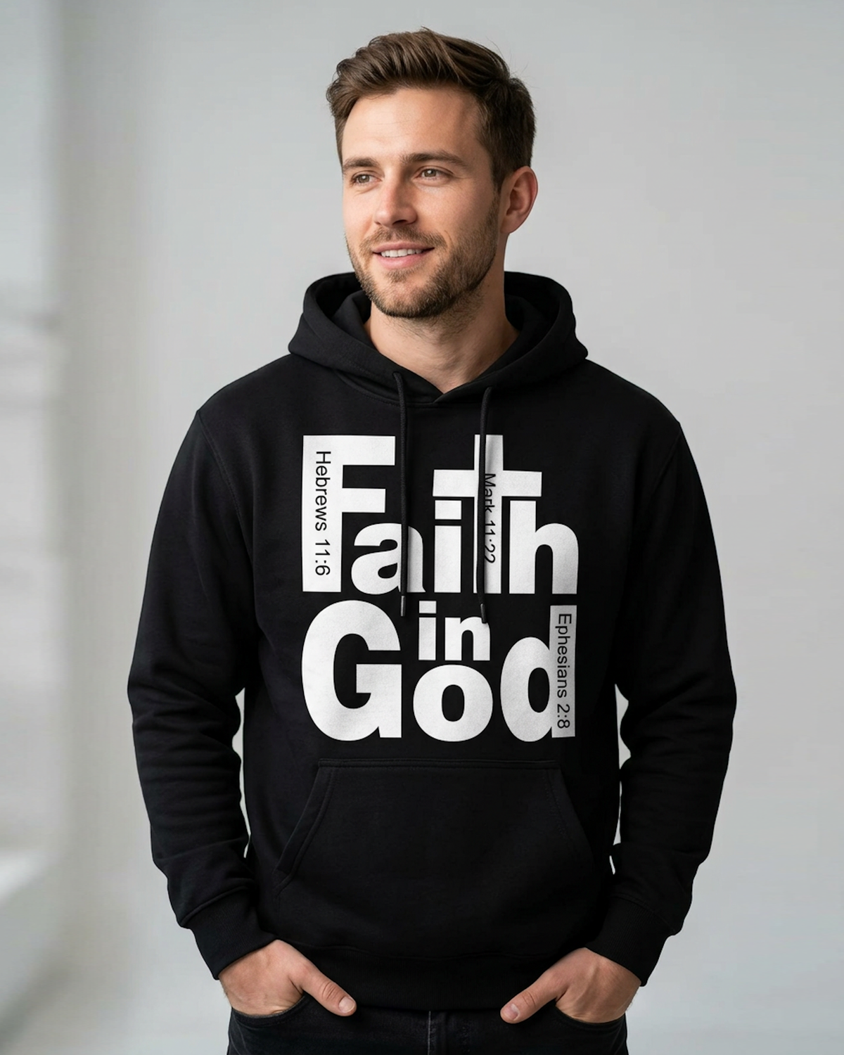 A man wearing a black pullover hoodie with a large white graphic print that reads 'Faith in God' with Bible verse references, posed inside a light gray walled room.