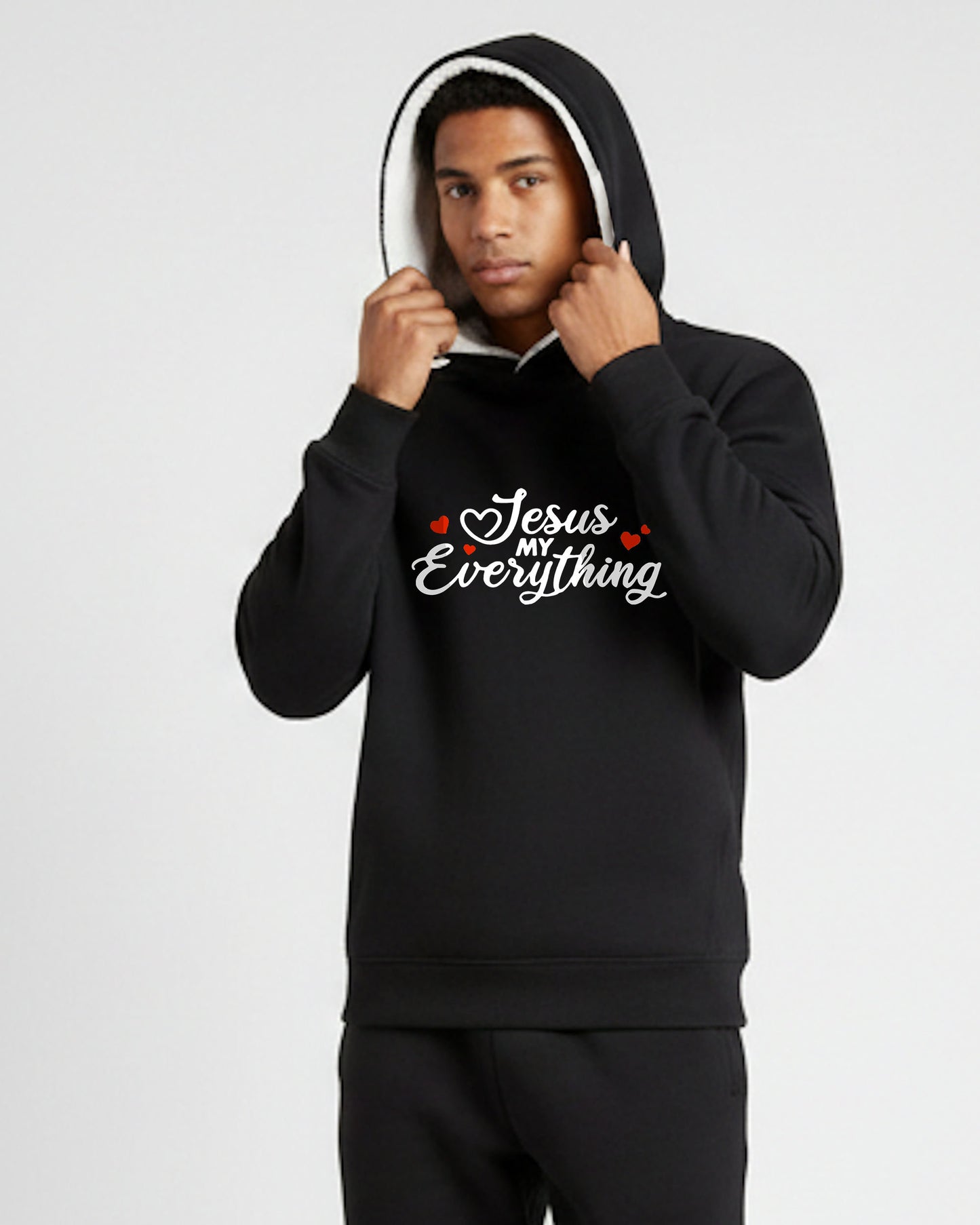 A man wearing a black hoodie with a Christian faith inspired text logo saying "Jesus My Everyhing" designed by Heavenly Dreamwear printed on the front.