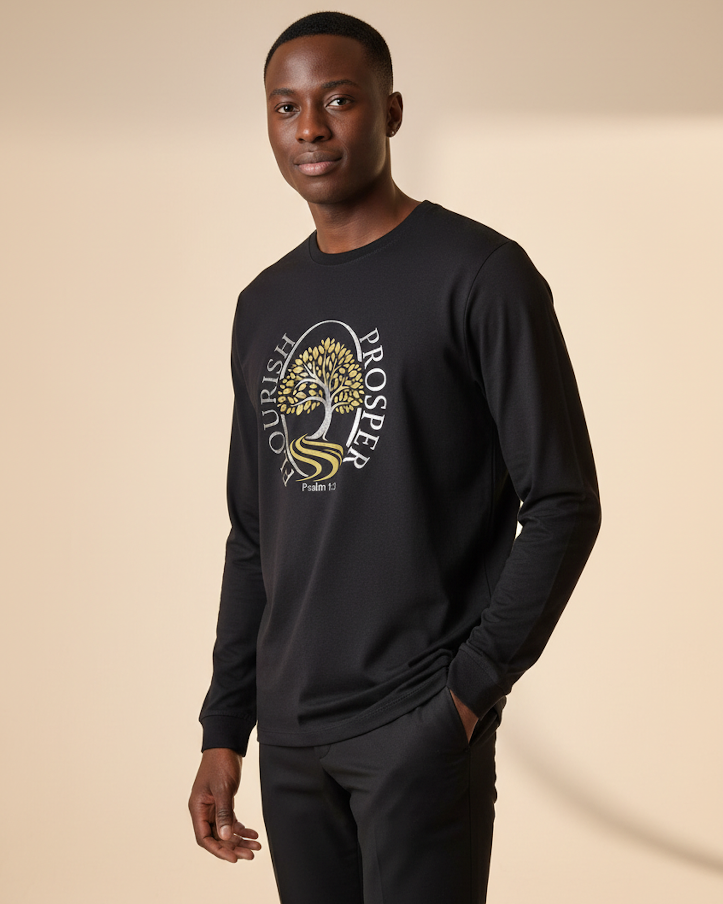 Man wearing  black long sleeve t-shirt with a gold and silver logo of a tree near a river with the text Flourish Prosper on the front against a beige background.