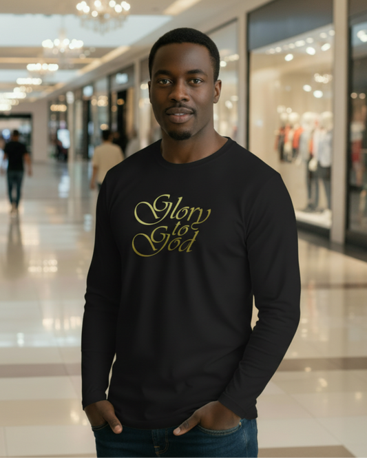 A man wearing a black long-sleeve t-shirt with 'Glory God' printed in gold cursive text on the chest, standing in a blurred shopping mall environment.