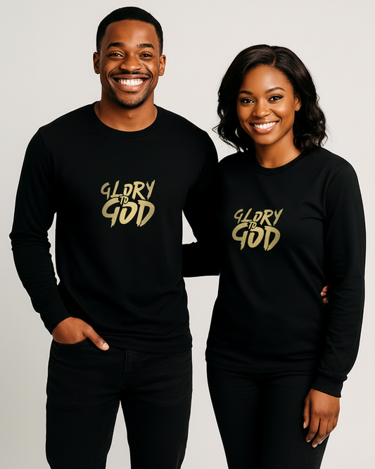 A smiling man and woman standing side by side wearing matching black long-sleeve shirts with a metallic gold 'GLORY TO GOD' graphic printed on the chest, against a plain light gray studio background.