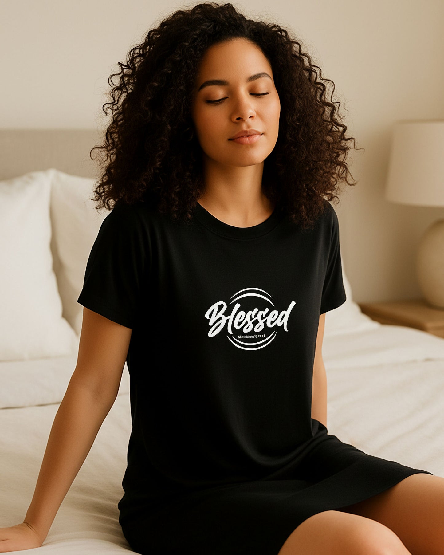 Woman wearing a black t-shirt dress with a white 'Blessed' logo in a bedroom setting