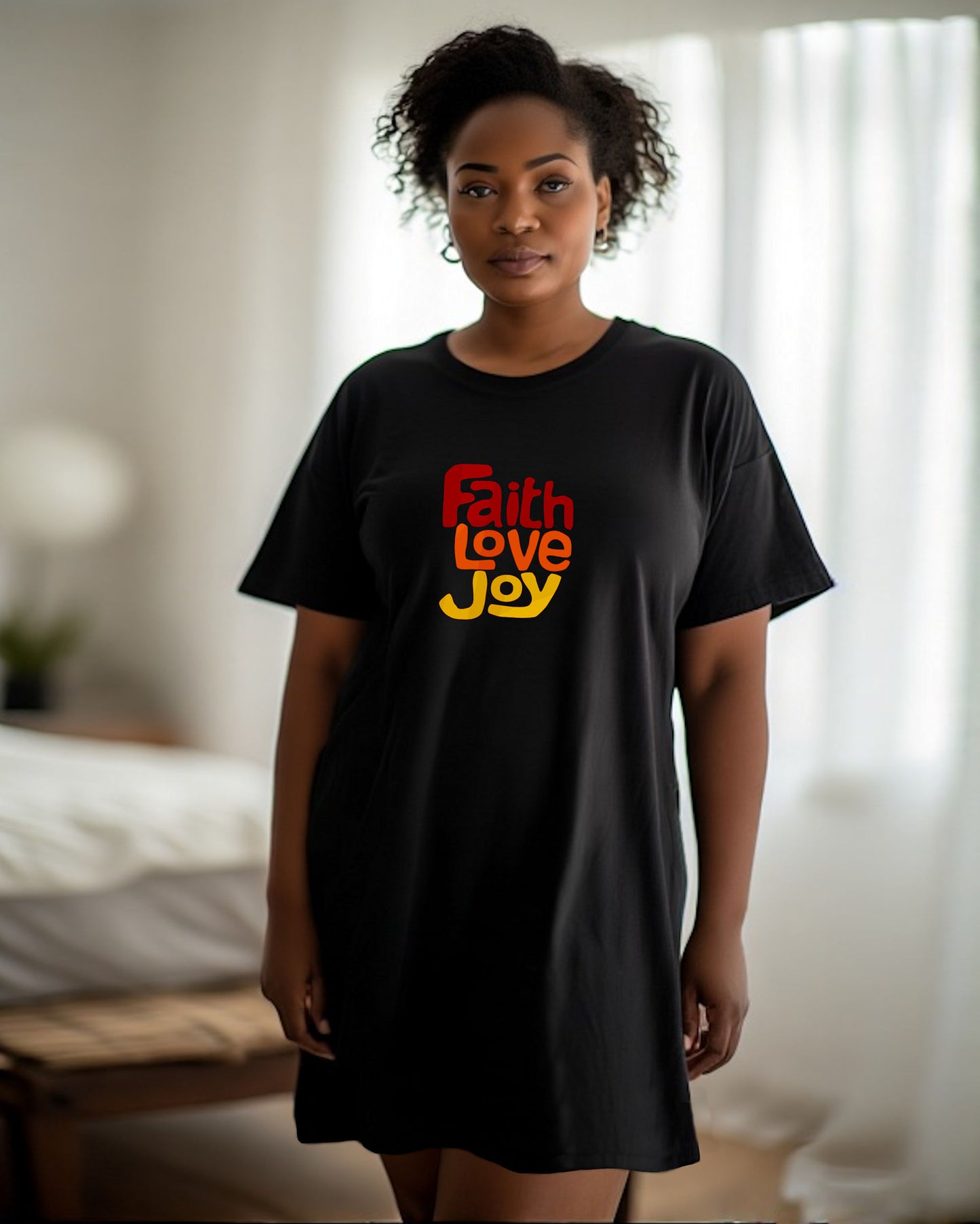 Woman wearing a black t-shirt nightdress with 'Faith Love Joy' text in red, orange, and yellow in a bedroom.