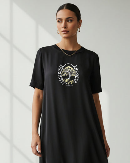 Woman in a bright room wearing a black t-shirt with a silver/gold logo.