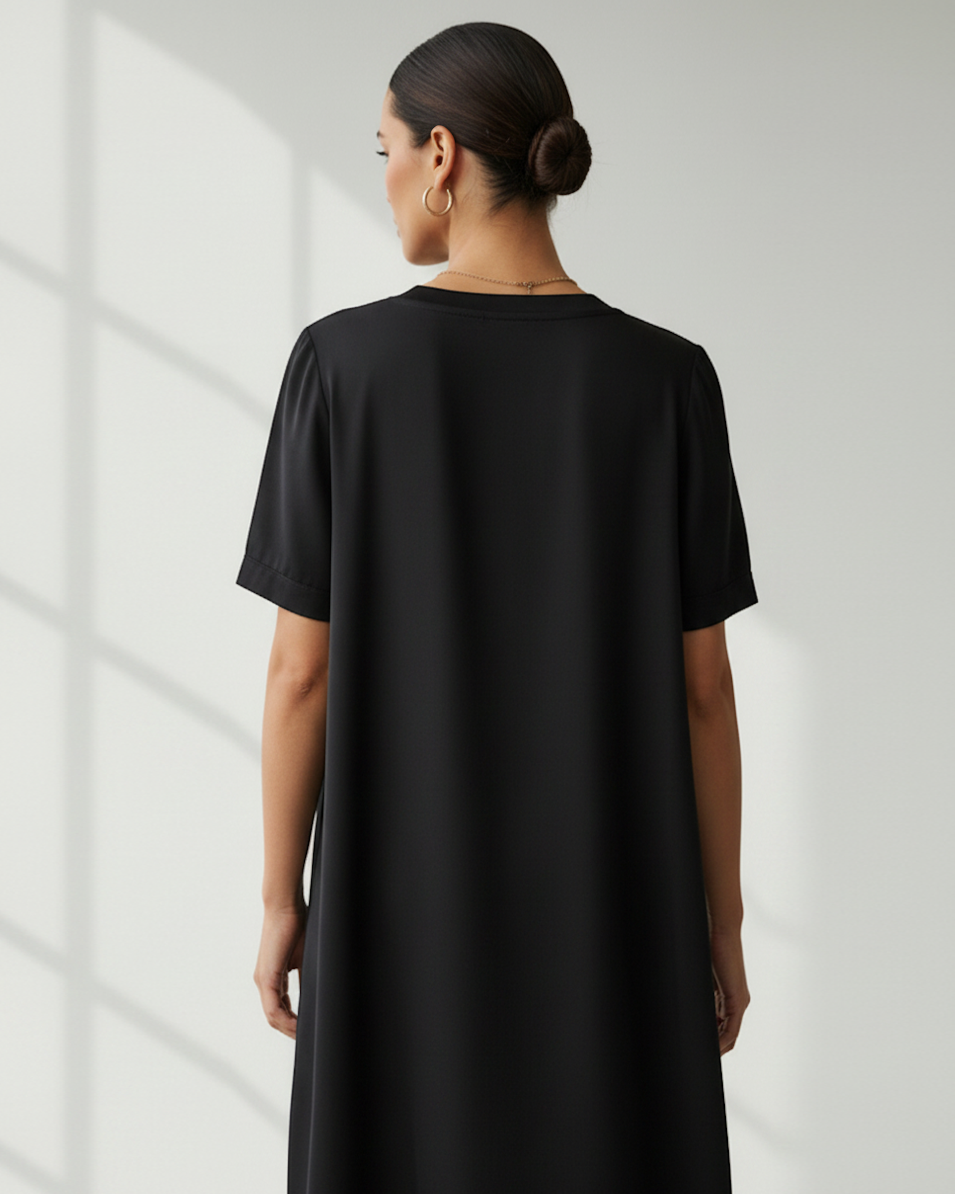 Rear view of a woman in a bright room wearing a black t-shirt dress.