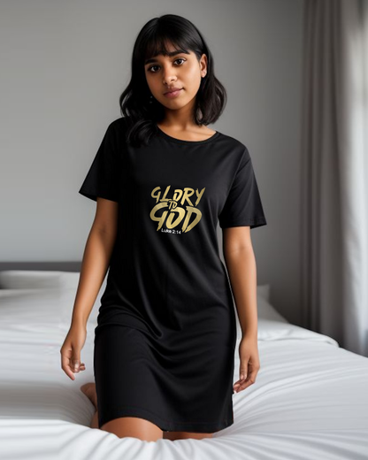 A woman in a bedroom wearing a black cotton t-shirt dress with a gold "Glory to God" logo printed on the front.