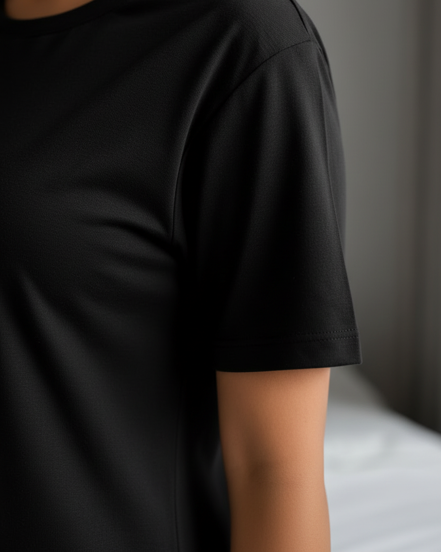 Sleeve of a black t-shirt dress worn by a woman in a bedroom.
