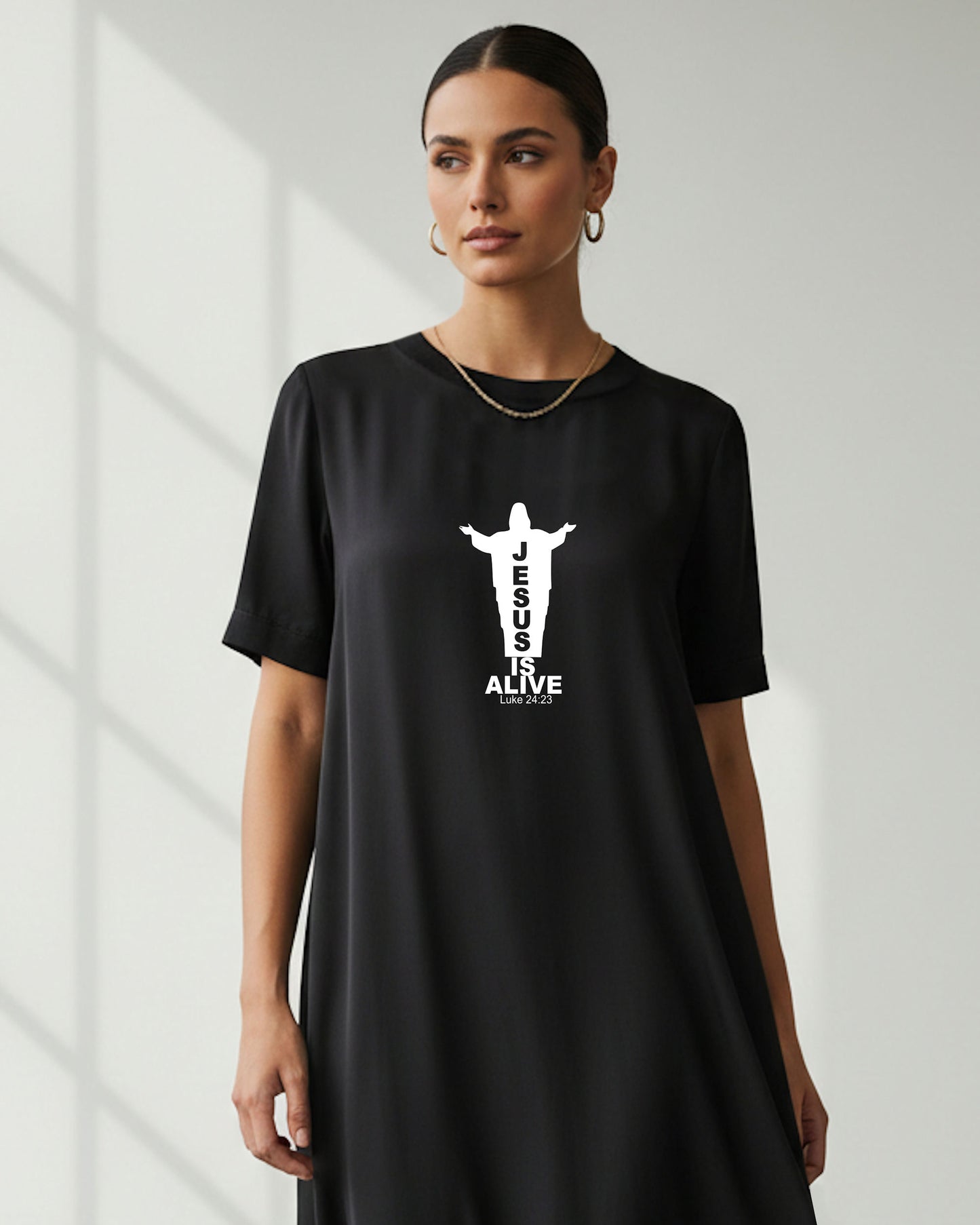 Woman wearing a black t-shirt dress with a white Jesus silhouette graphic and text, standing indoors.