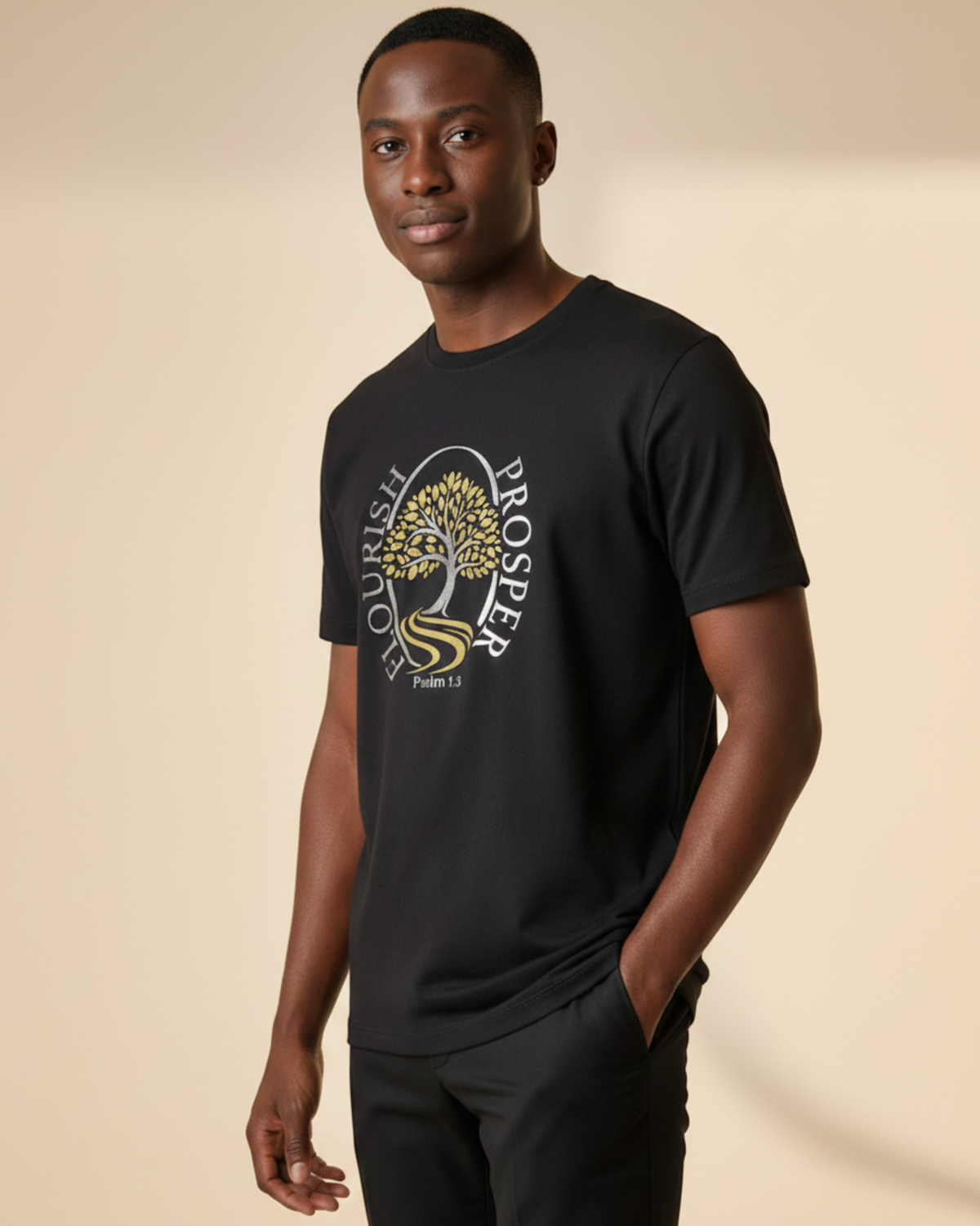 A man wearing a black crewneck t-shirt with a gold and silver graphic on the chest, posed against a solid beige studio background.