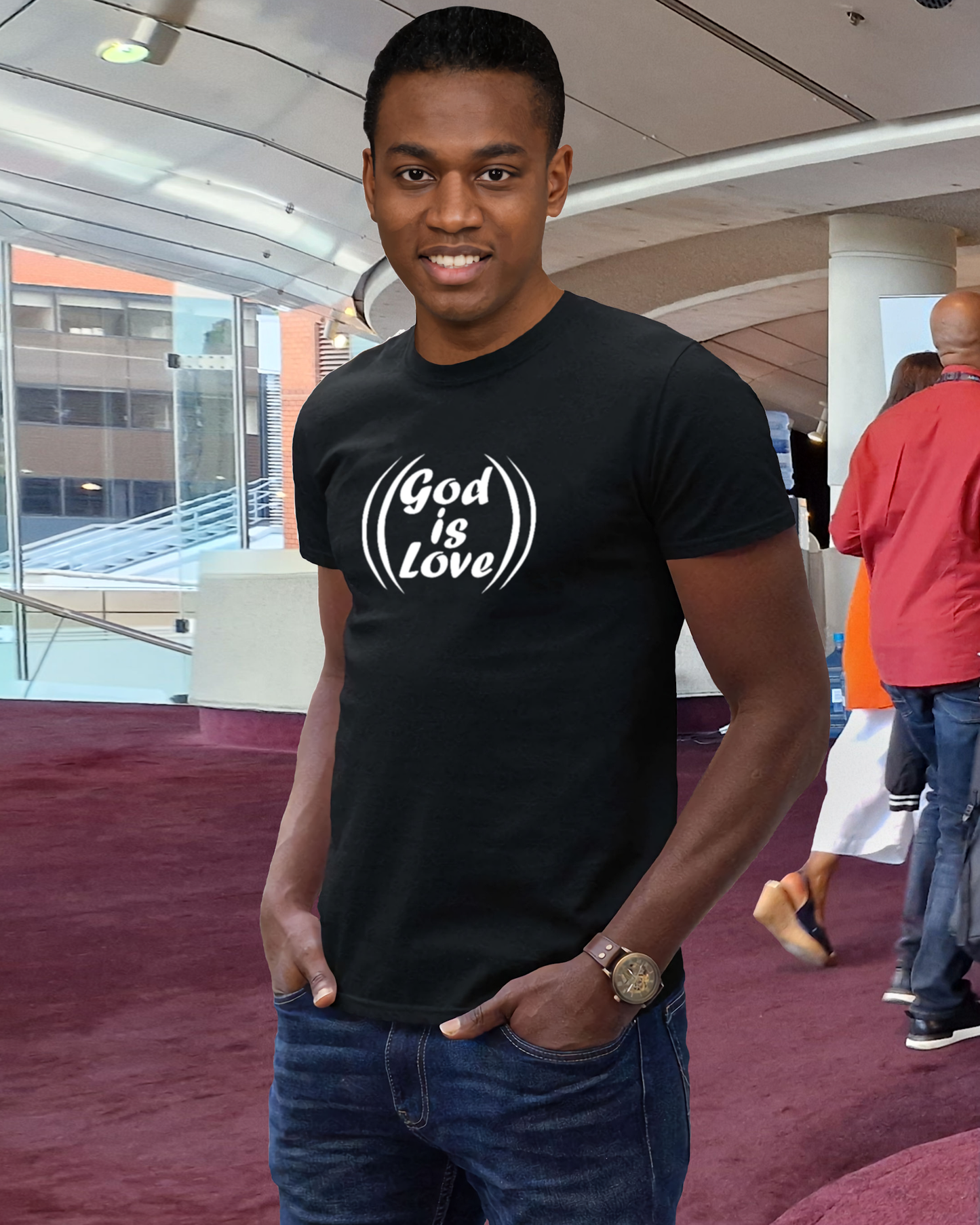 A man in a conference centre wearing a black t-shirt with a white "God is Love" logo printed on the front.