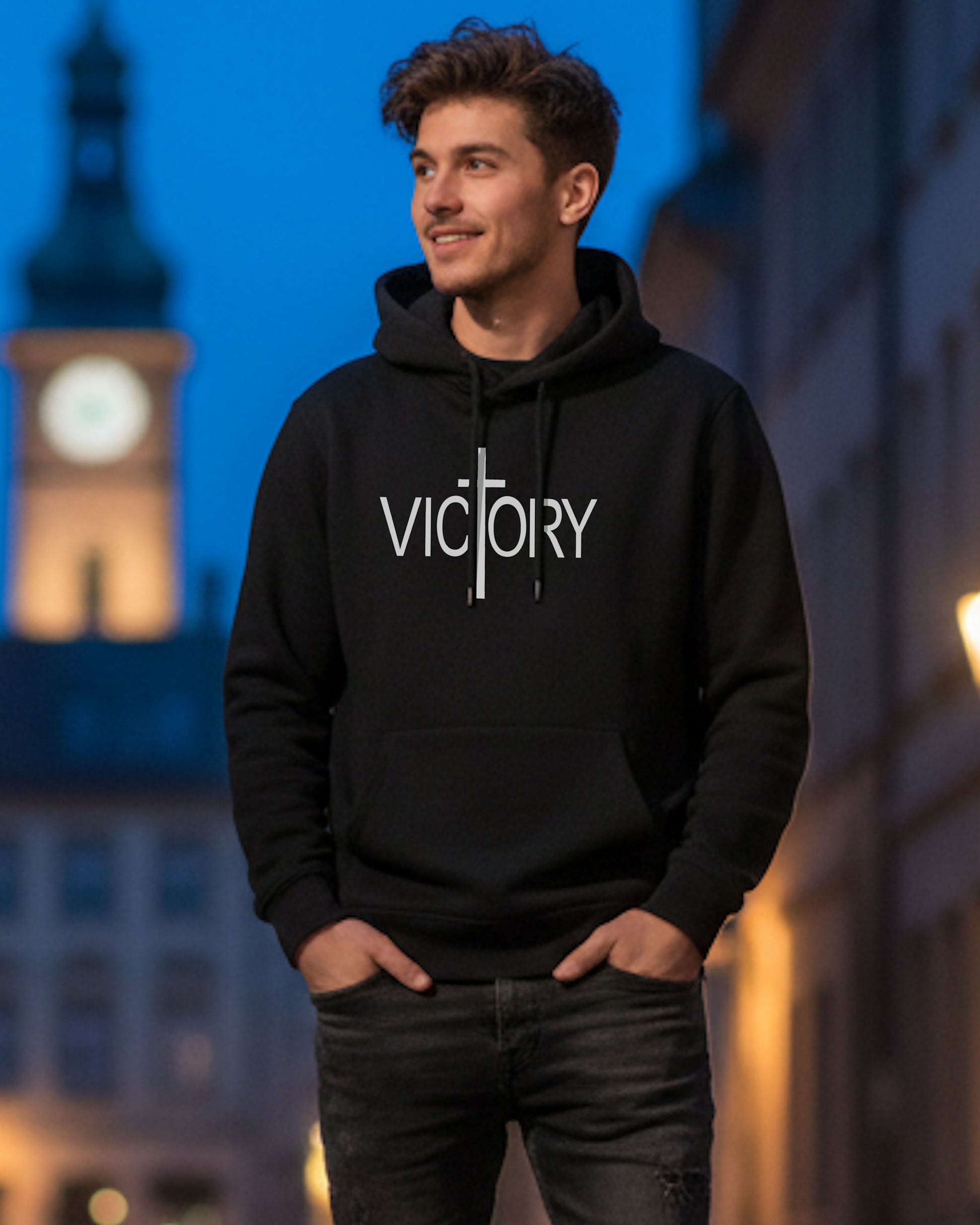 A young man in a street wearing a black hoodie with a white Heavenly Dreamwear "Victory" logo printed on front.