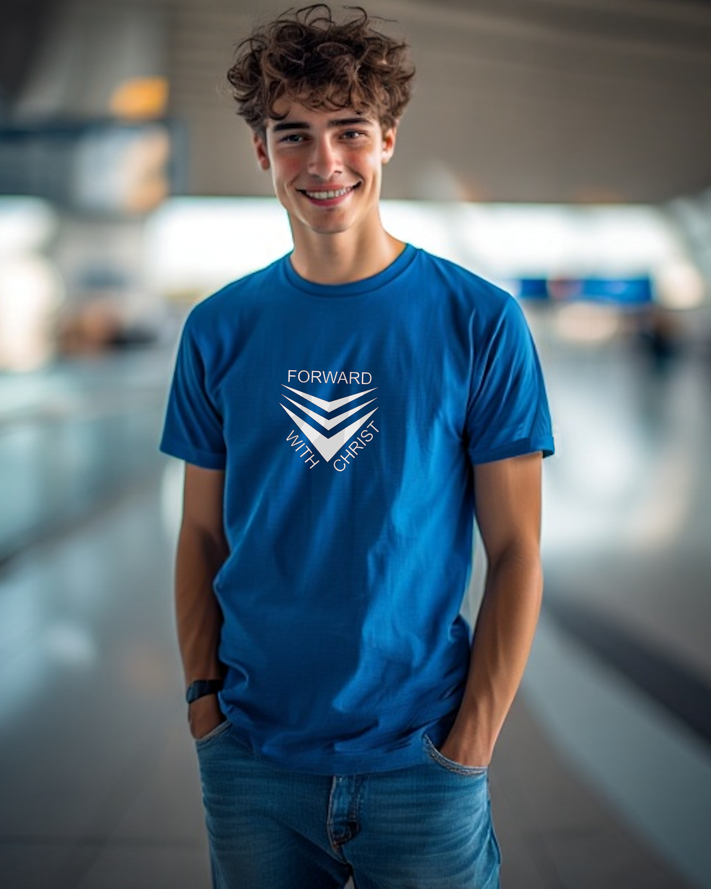 A man standing in an airport wearing a blue short sleeve t-shirt that has a white logo with the words "FORWARD WITH CHRIST" around 3 downward pointing chevrons.