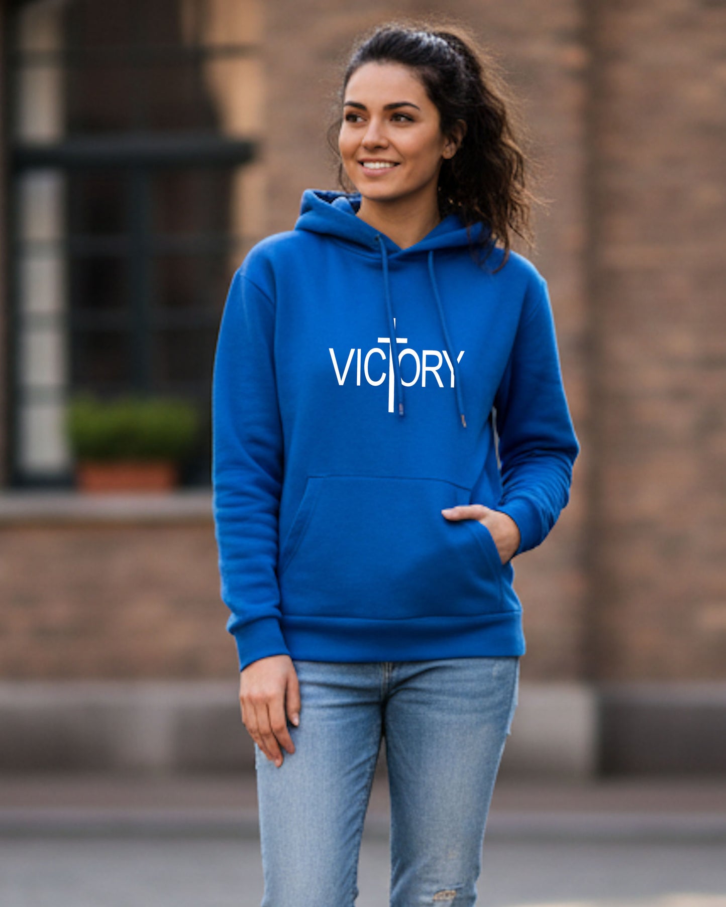 A younge woman in a street wearing a blue hoodie with a white Heavenly Dreamwear "Victory" logo printed on front.
