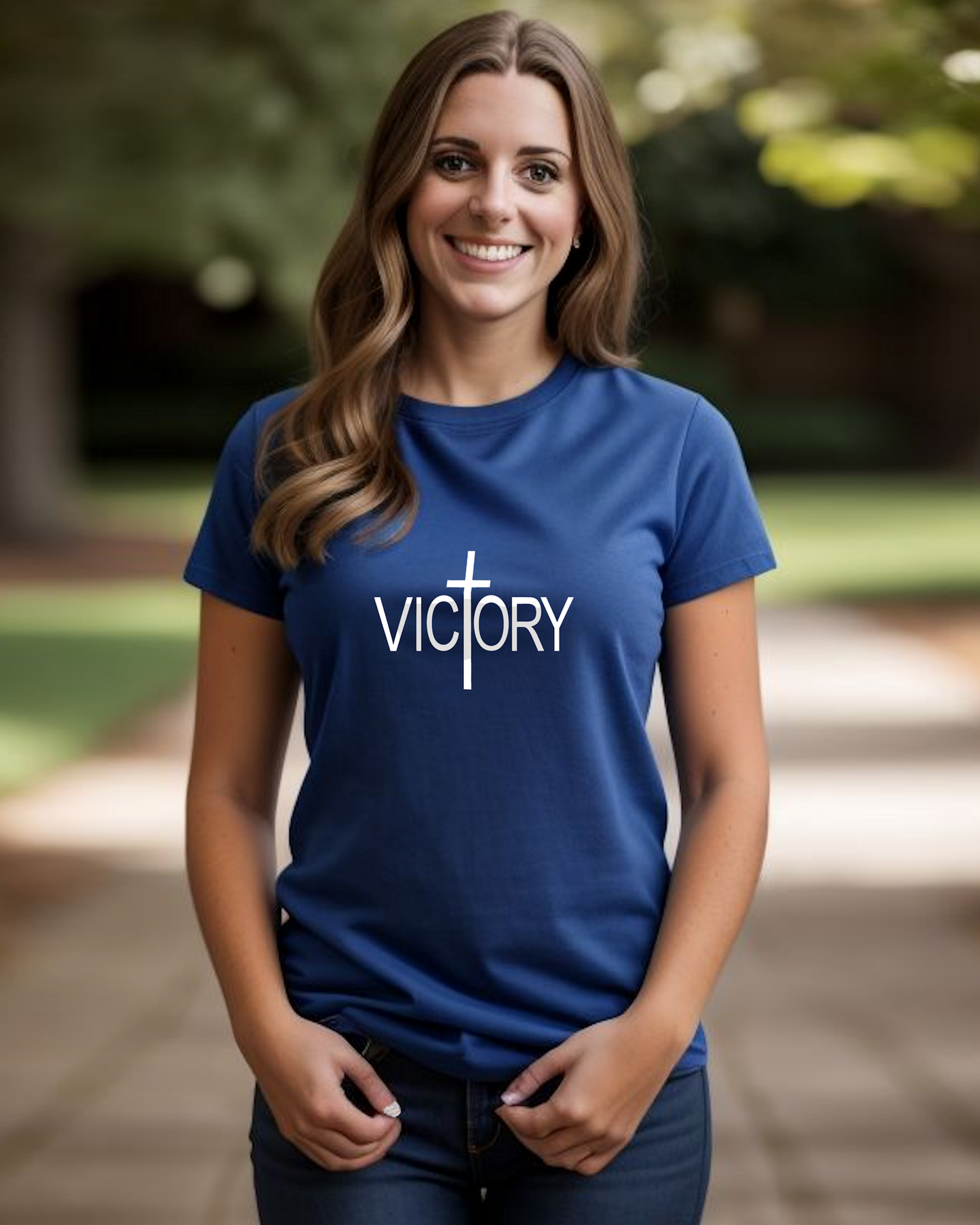 A woman wearing a blue t-shirt with a white Heavenly Dreamwear "Victory" logo printed on the front, standing in a garden.