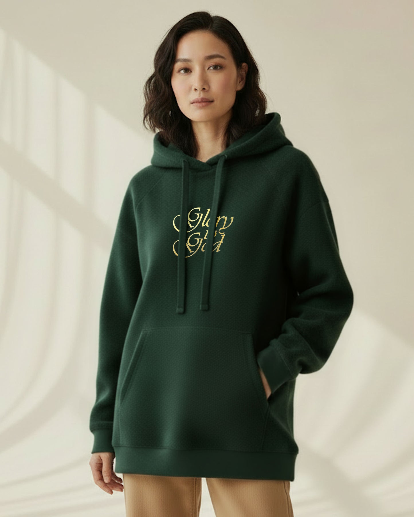 Person wearing a dark green hoodie with a gold text logo, 'Glory to God' on a neutral background