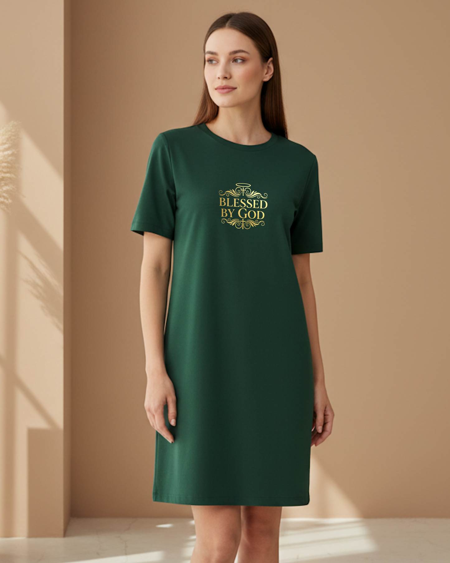 Woman standing indoors wearing a dark green t-shirt dress with 'Blessed by God' text in gold.