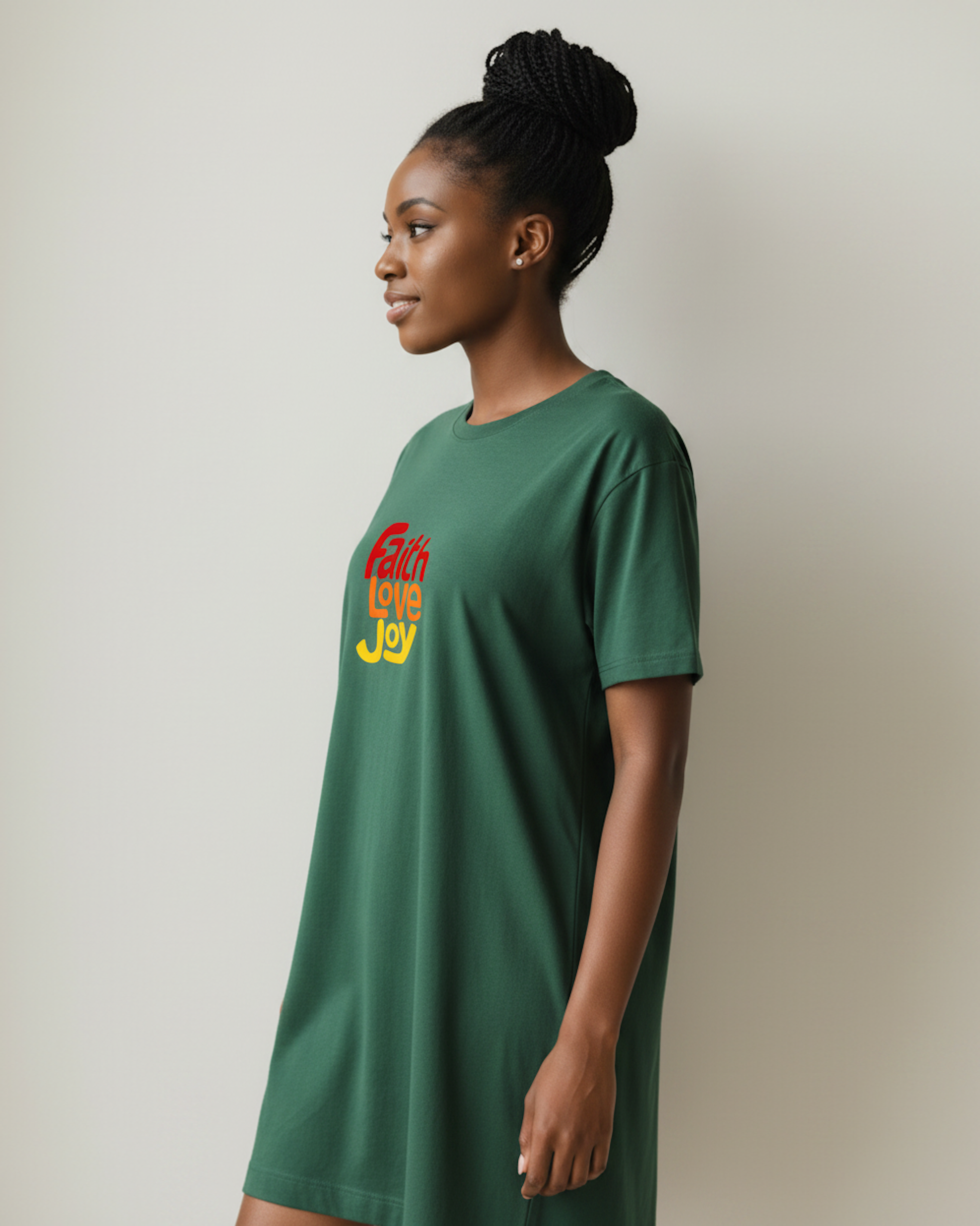 Side view of a woman wearing dark green t-shirt dress with a colourful Faith Love Joy logo printed on the front in red, orange and yellow against a beige background.
