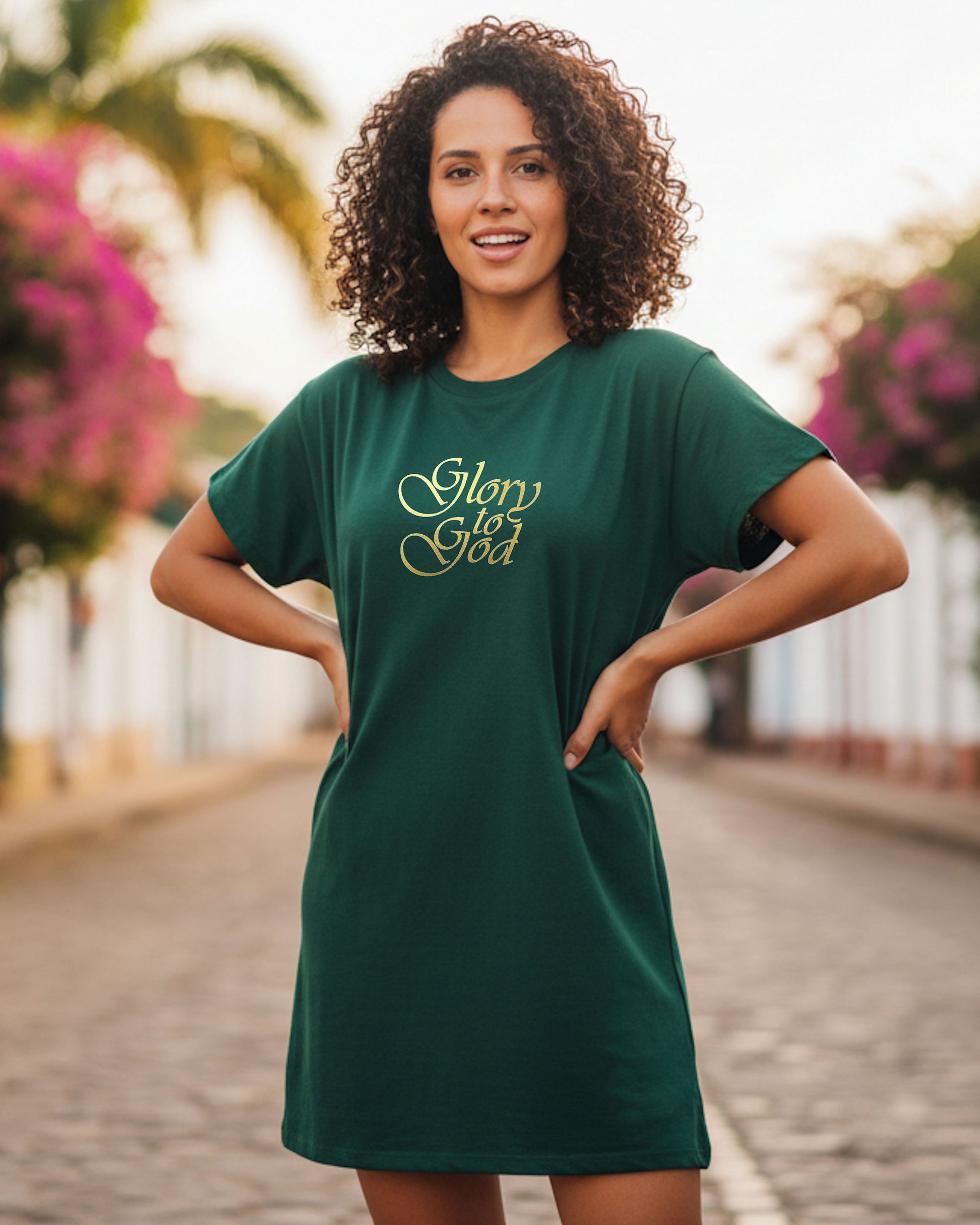 A woman in a street wearing a dark green t-shirt dress with gold text the says, 'Glory to God'