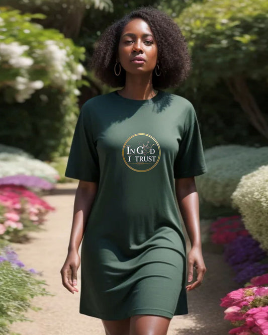 Woman in a garden wearing a dark green t-shirt dress with a gold ring logo and white text 'In God I Trust'