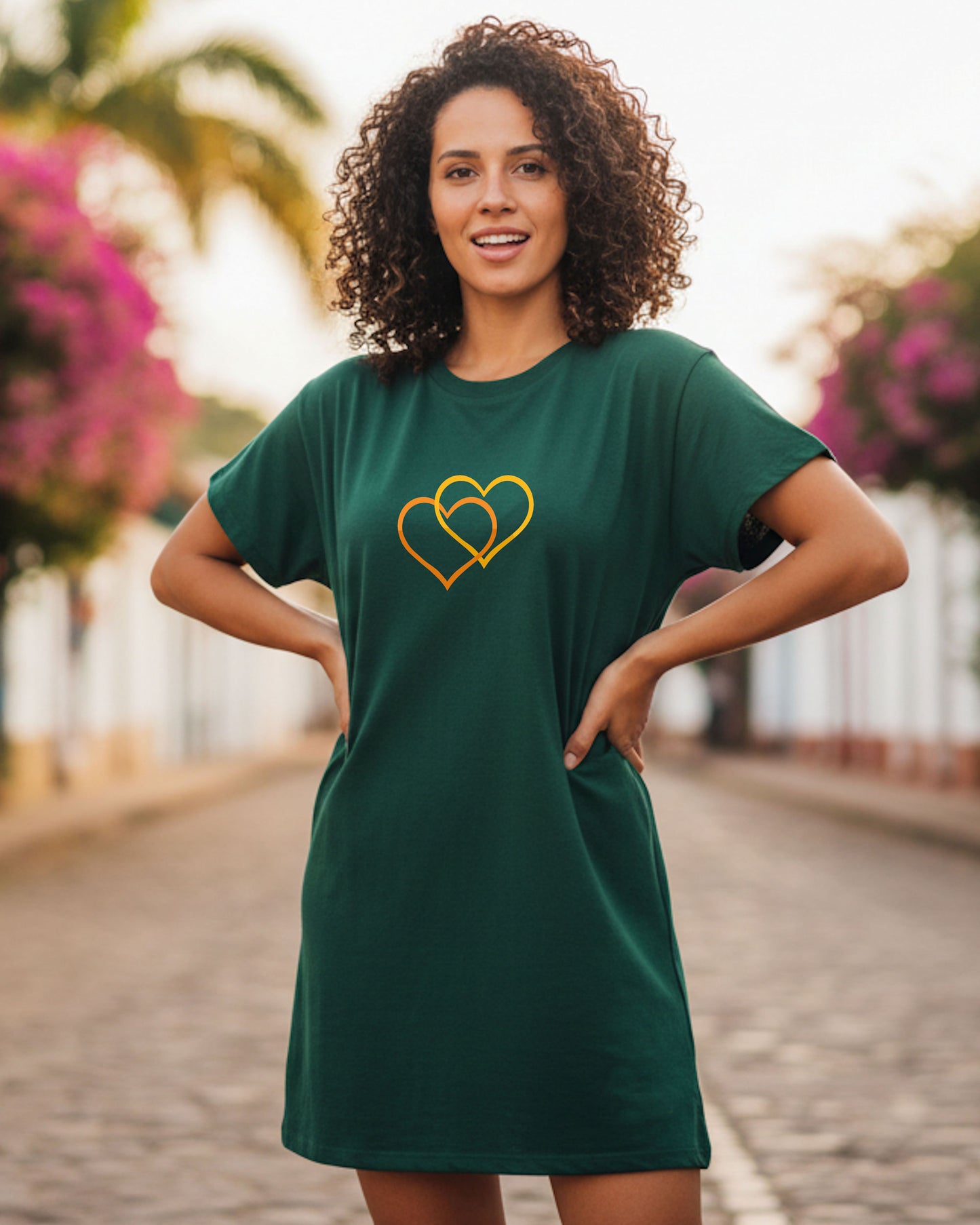Woman wearing a dark green t-shirt dress with a orange/yellow dual heart logo design outdoors.