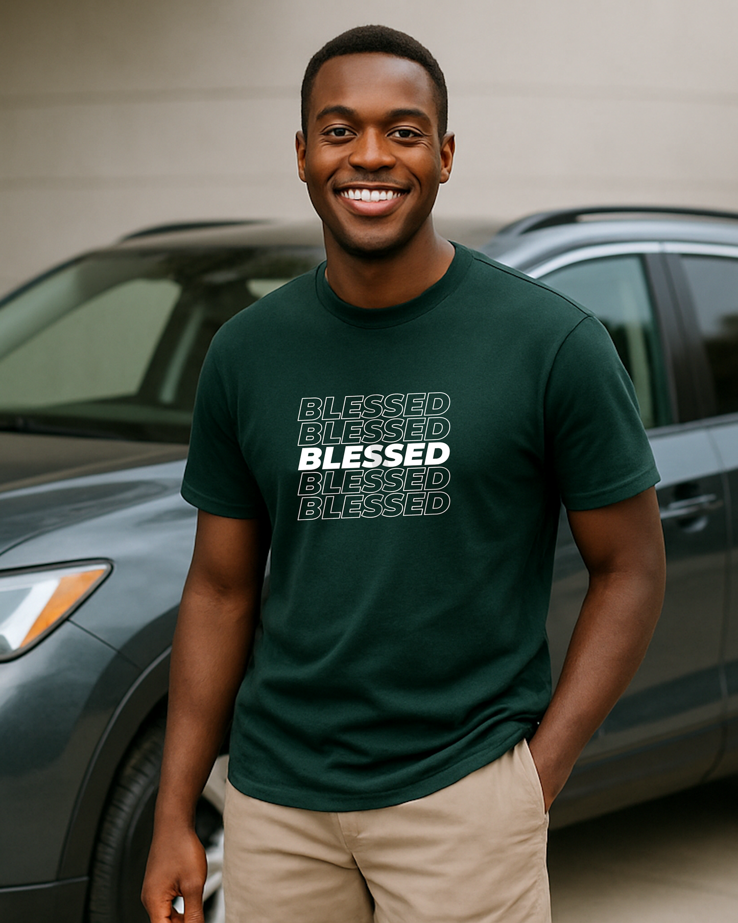 A young man in a garage wearing a dark green t-shirt with multiple lines of "Blessed" text printed on the front.