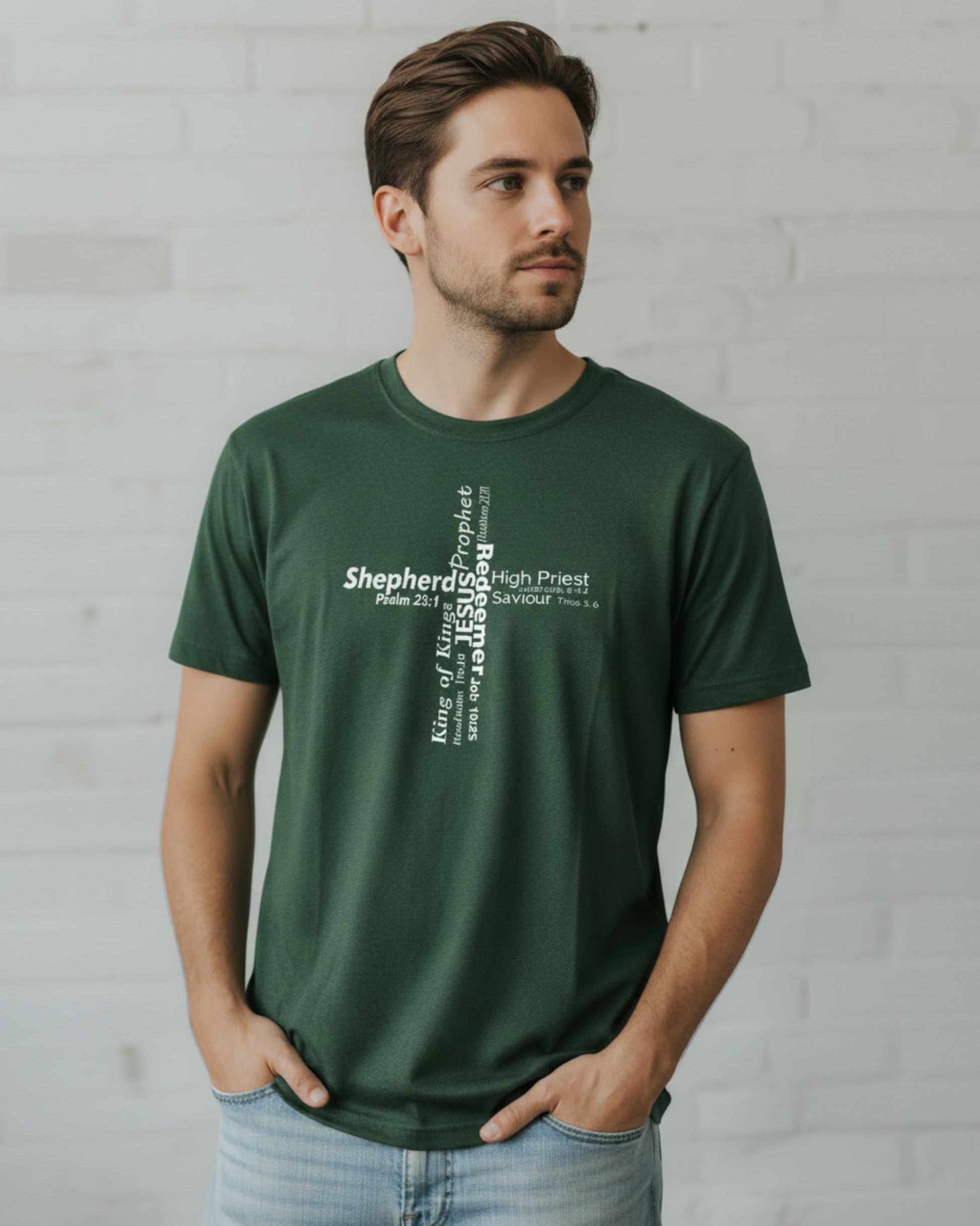 A man wearing a dark green short-sleeve t-shirt against a plain light gray wall. The front of the shirt features a vertical white text graphic reading 'Shepherd of Kings, Prophets, High Priest, Jesus' with biblical references.