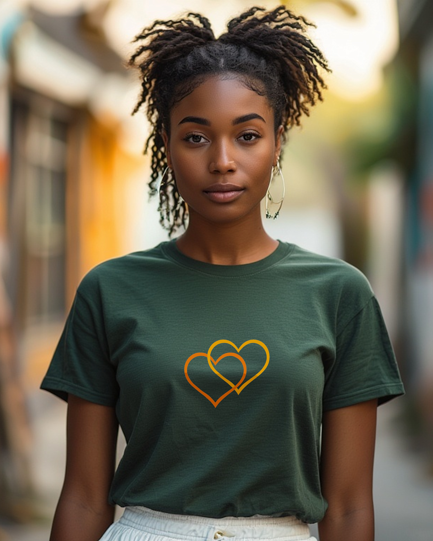 A woman in a street wearing a dark green t-shirt with a Heavenly Dreamwear logo comprised of an orange and yellow inter-twinned hearts.