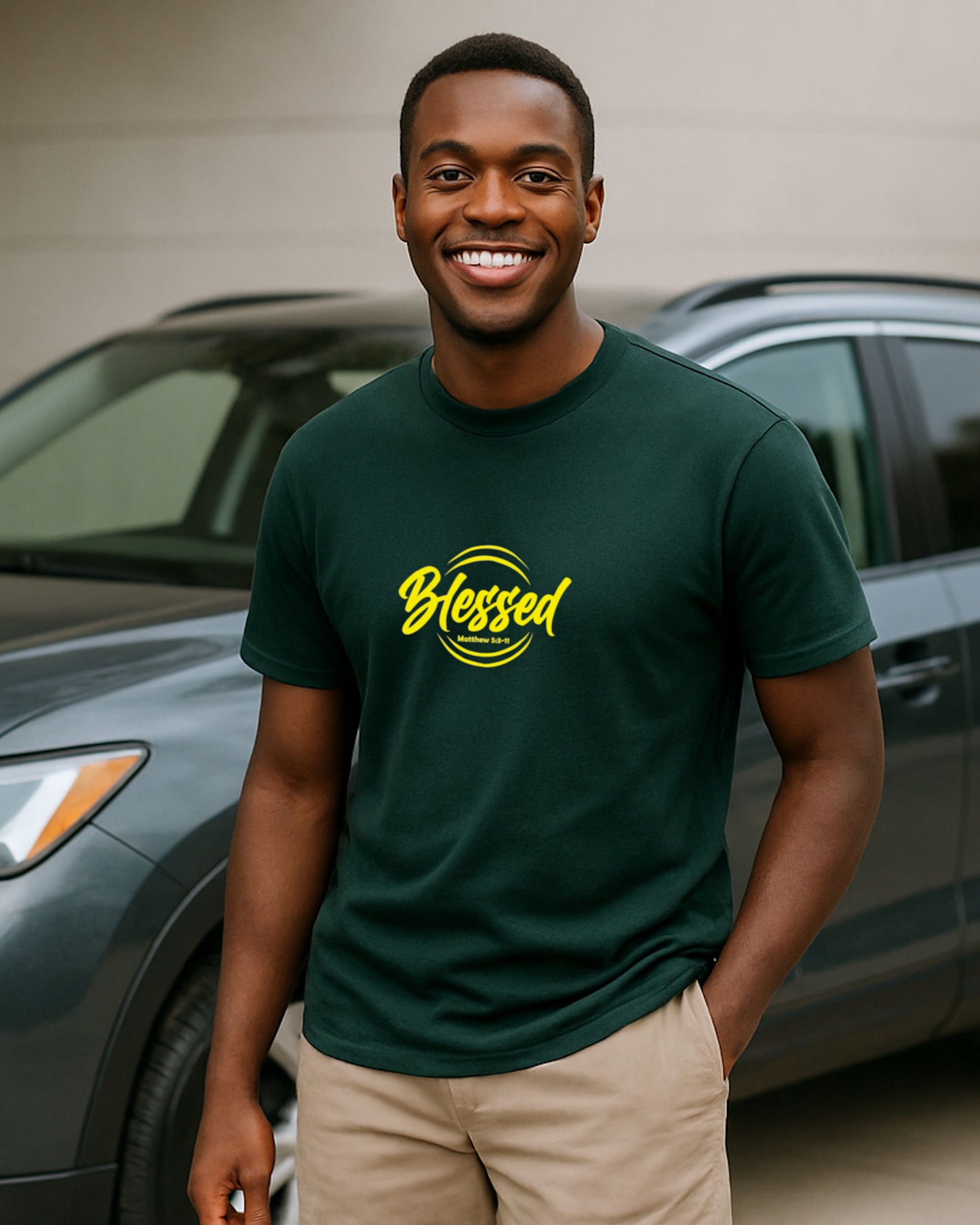 A young man wearing a green faith-based t-shirt with a yellow text Heavenly Dreamwear  logo that says 'Blessed' standing next to a car.