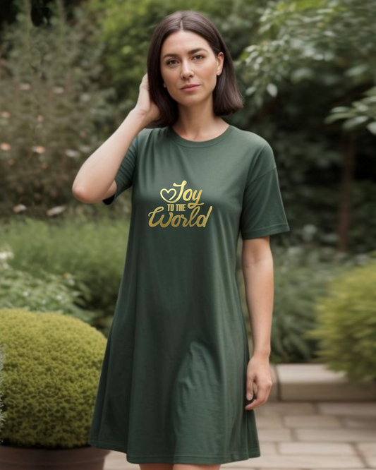 A woman standing in a garden wearing a dark green Heavenly Dreamwear t-shirt dress with a gold "Joy to the World" logo printed on the front.