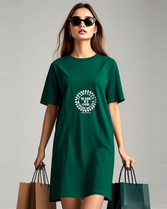 A woman carrying shopping bags wearing a dark green t-shirt dress with a white Heavenly Dreamwear logo comprised of  text "Fearfully Wonderfully Made by God" inside a geared wheel.