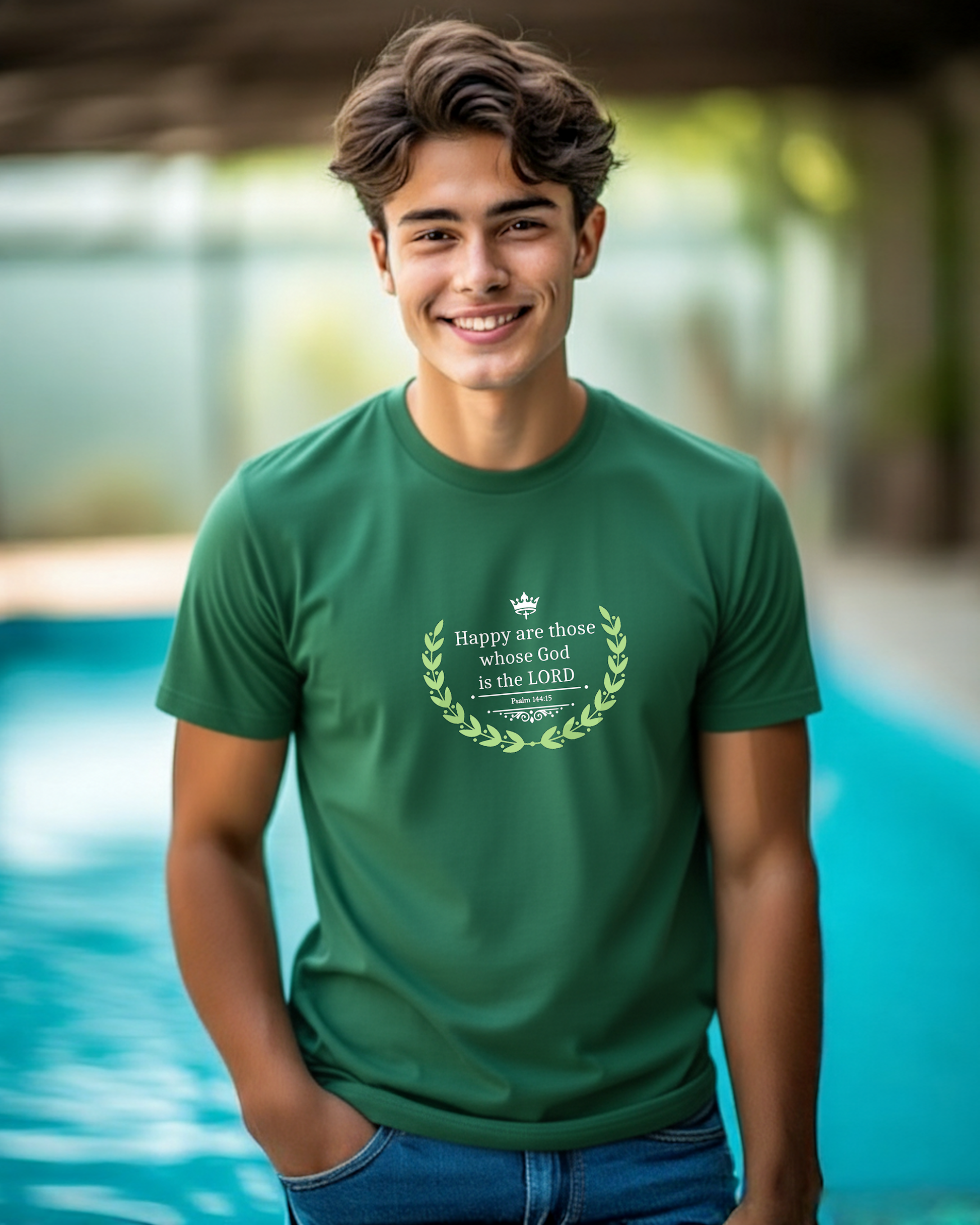 A smiling young man wearing a green graphic t-shirt with a white laurel wreath and text reading 'Happy are those whose God is the LORD', standing in front of a blurred swimming pool background.