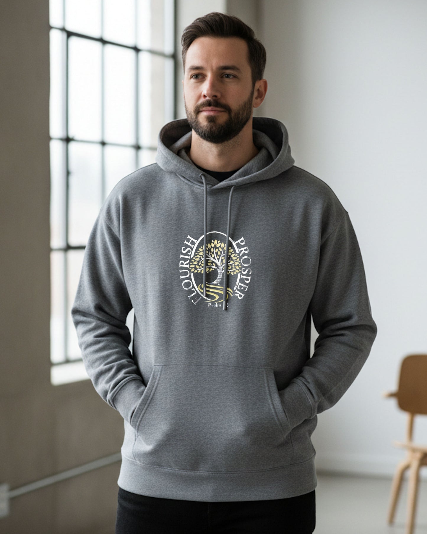 Man indoors wearing a grey hoodie with a gold/silver logo and text, 'Flourish Prosper'