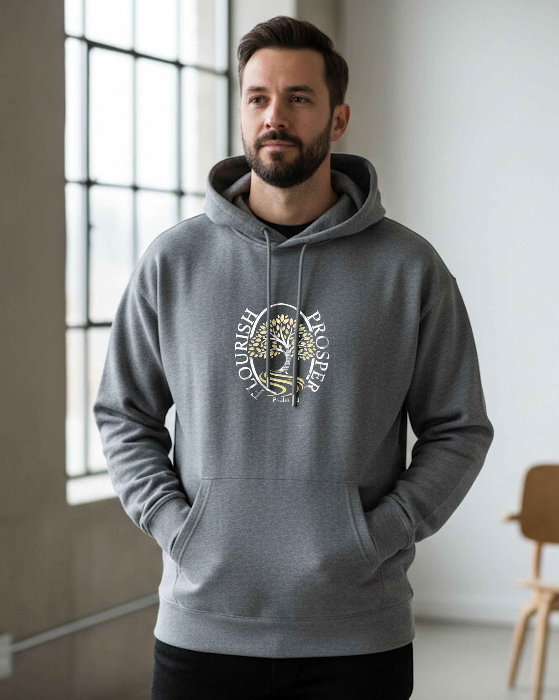 Man indoors wearing a grey hoodie with a gold/silver logo and text, 'Flourish Prosper'