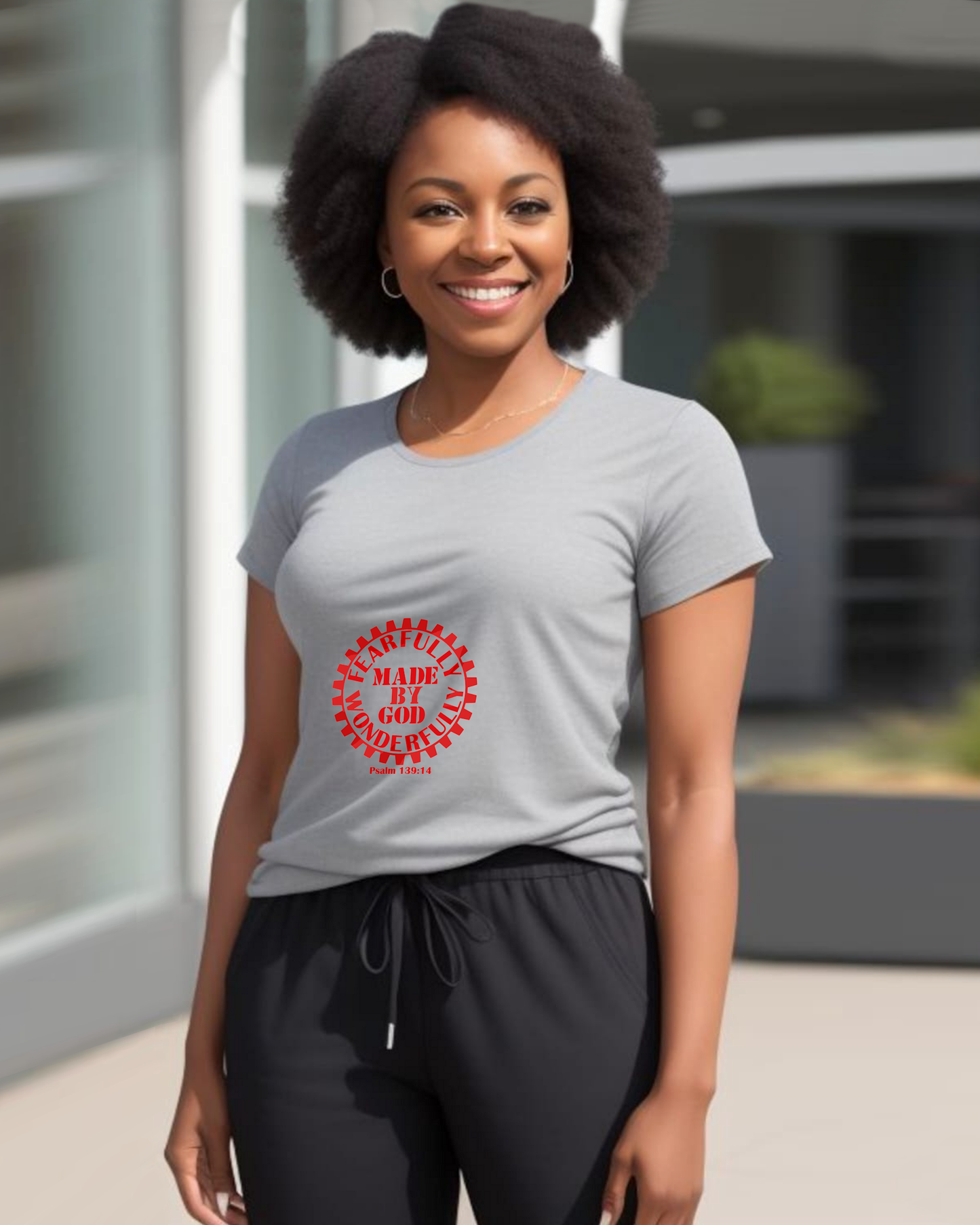 A woman standing in a garden wearing a grey t-shirt with a red Heavenly Dreamwear logo with the text "Fearfully Wonderfully Made by God" inside a geared wheel.