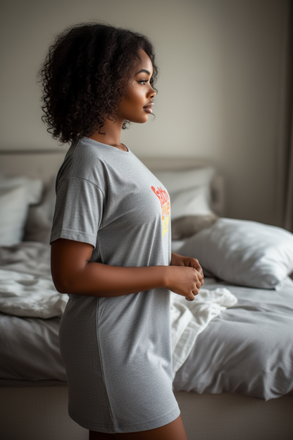Woman wearing a grey t-shirt dress with a red, orange, and yellow logo in a bedroom.